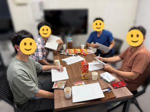 机を囲んで本を開く4名の男性の写真